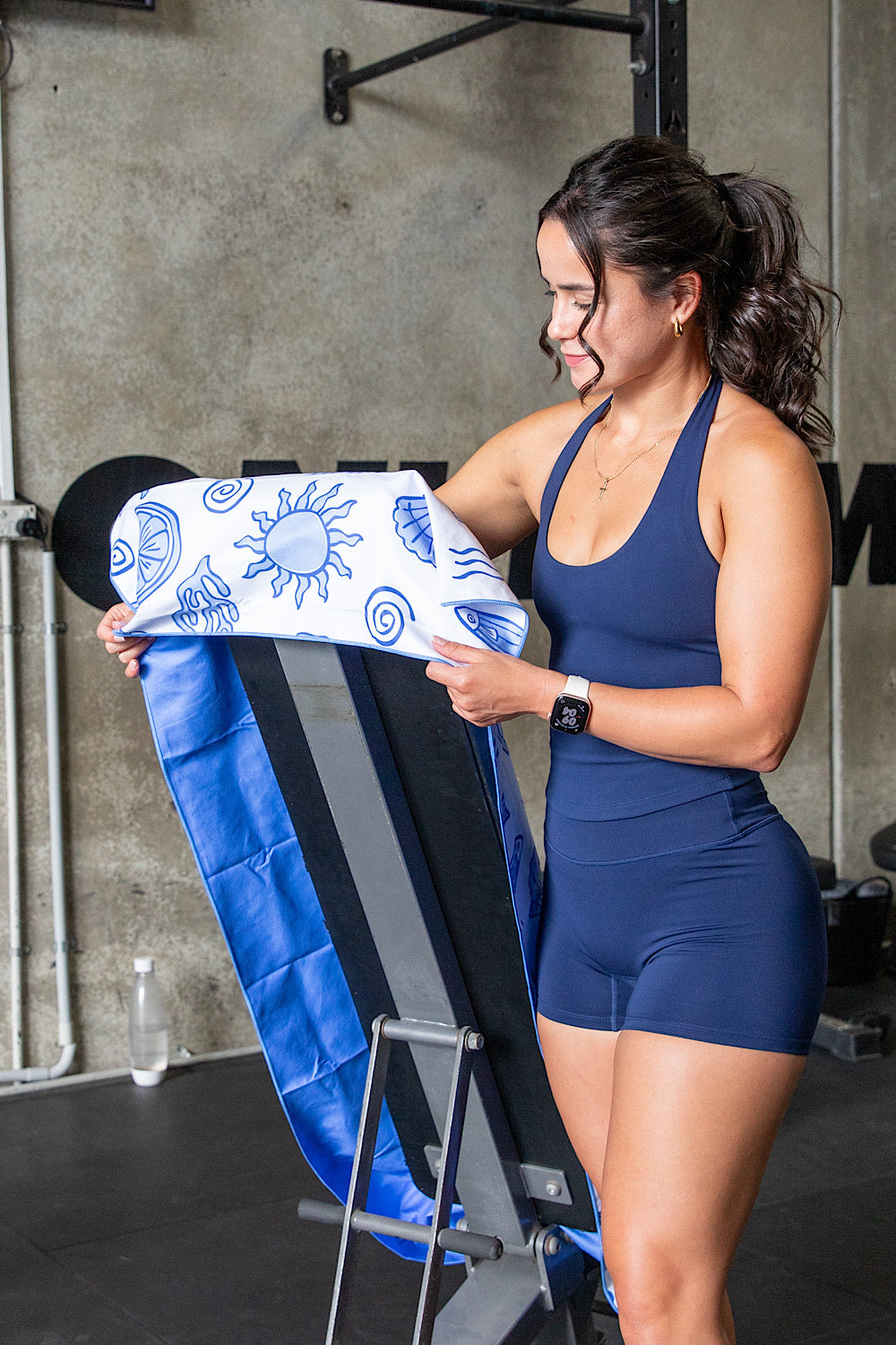 Woman in blue athletic wear holding a white towel with blue patterns in a gym setting.