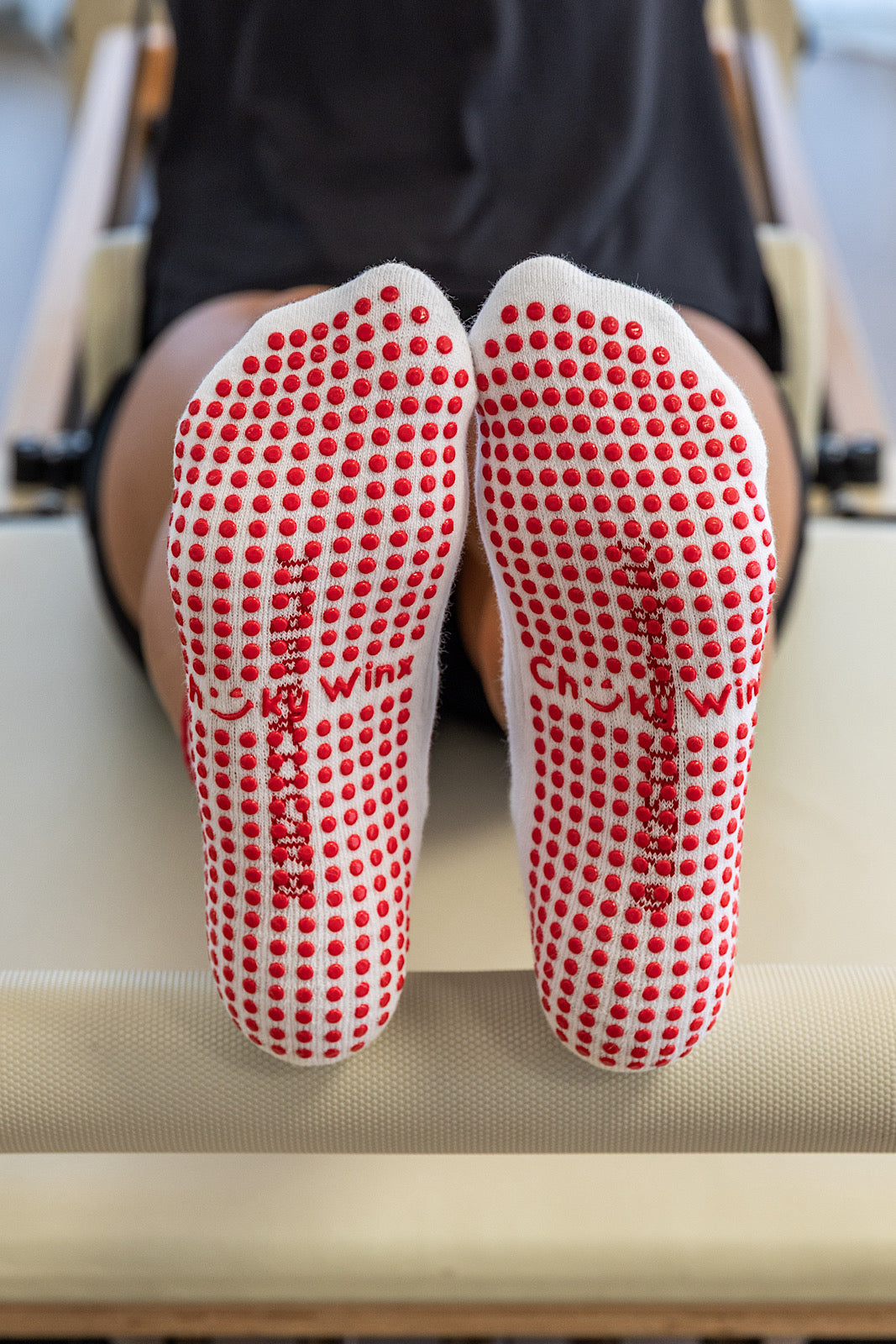 White grips socks with red dots worn by a person sitting on a reformer